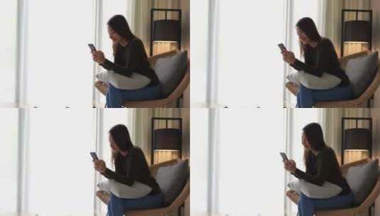 年轻的亚洲女人穿着牛仔裤和栗色毛衣坐在一把前倾的大藤椅上高清在线视频素材下载