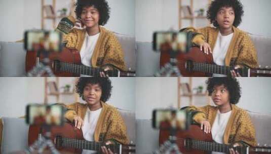 美丽的美国年轻女子将手机放在三脚架上并录制视频封面弹吉他和唱歌高清在线视频素材下载