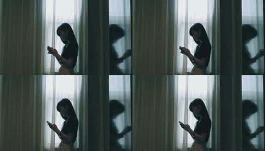女孩在窗边玩手机发信息剪影高清在线视频素材下载