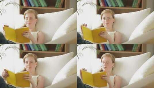 美丽的金发女孩放松的躺在沙发上看书高清在线视频素材下载