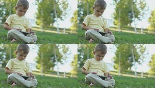小男孩坐在草坪上玩平板高清在线视频素材下载