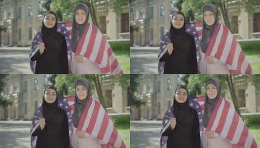 两名裹着美国国旗的穆斯林妇女看着镜头微笑。自信的肖像高清在线视频素材下载