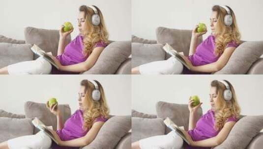 漂亮的年轻女人戴着耳机吃着苹果躺在沙发上看书高清在线视频素材下载