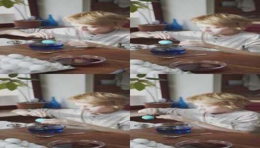 一个男孩从一碗蓝色液体中舀出彩色的鸡蛋竖屏高清在线视频素材下载