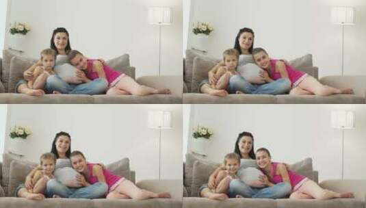 怀孕的女人和她的两个女儿坐在沙发上对着镜头微笑高清在线视频素材下载