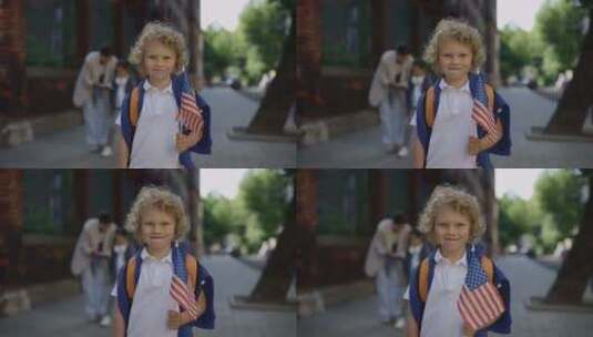 拿着美国国旗站在学校附近的小男孩肖像高清在线视频素材下载