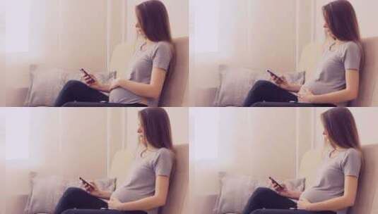 坐在沙发上的孕妇在使用手机高清在线视频素材下载