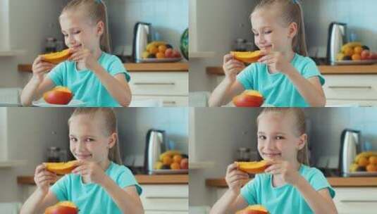 女孩坐在厨房的桌子前吃芒果高清在线视频素材下载