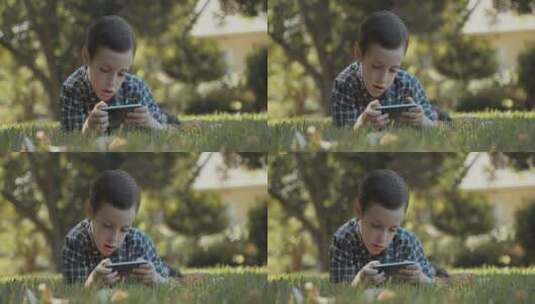 男孩趴在草坪上玩手机高清在线视频素材下载