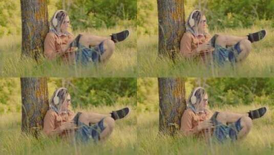 戴眼镜耳机的年轻人在夏天坐在树旁看书高清在线视频素材下载