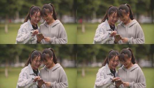 两位女大学生在校园草地上看手机网购学习高清在线视频素材下载