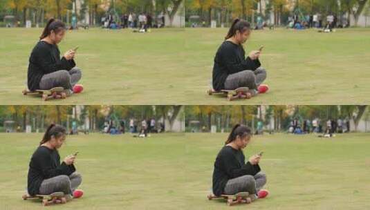 大学校园草地上女大学生坐在滑板上玩手机高清在线视频素材下载